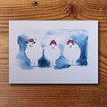 Weihnachtskarte mit drei Aquarell-Schafen in roten Weihnachtsmützen auf blauem Hintergrund